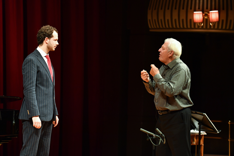 A man talking to male student, dressed in a suit, on stage, with a microphone in between them.